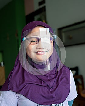 A young girl in hijab wearing the face protection shield. A safety face shield corona mask during Covid-19 pandemic