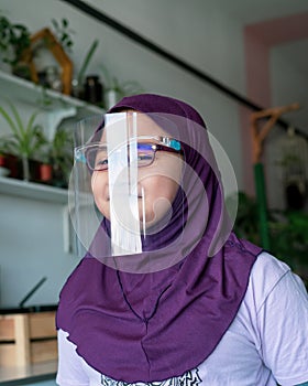 A young girl in hijab wearing the face protection shield. A safety face shield corona mask during Covid-19 pandemic