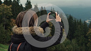 Young girl hiker is shooting video of beautiful misty mountain landscape on mobile phone camera.