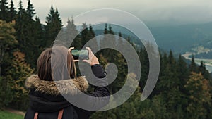 Young girl hiker is shooting video of beautiful misty mountain landscape on mobile phone camera.