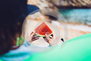 Young girl hipster relax on beach coast and holds in her hand a slice of red fresh fruit watermelon on blue sea background, woman