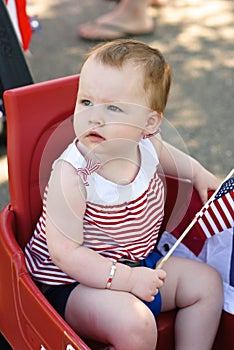 Young girl holding an American flag and riding in red wagon having fun in the park for July Fourth