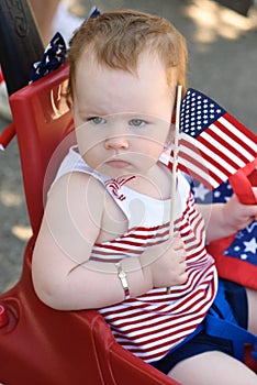 Young girl holding an American flag and riding in red wagon having fun in the park for July Fourth