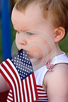 Young girl holding an American flag and riding in red wagon having fun in the park for July Fourth