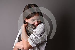 Young girl holding a baby cat on gray background. Female hugging her cute kitty. Adorable domestic pet concept.