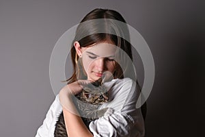 Young girl holding a baby cat on gray background. Female hugging her cute kitty. Adorable domestic pet concept.