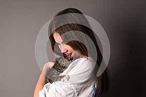 Young girl holding a baby cat on gray background. Female hugging her cute kitty. Adorable domestic pet concept.