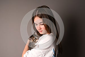 Young girl holding a baby cat on gray background. Female hugging her cute kitty. Adorable domestic pet concept.