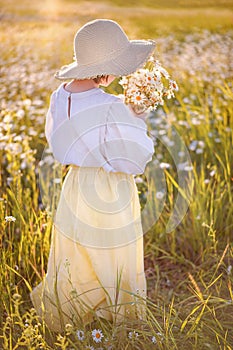 Young girl holding bunch of chamomile on the summer field