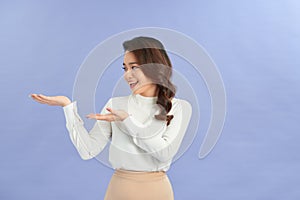 Young girl holding copyspace imaginary on the palm to insert an ad on purple background