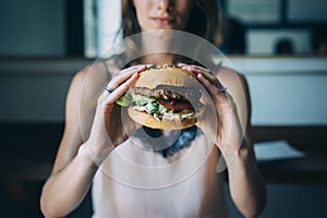 Young girl holding in female hands fast food burger, american unhealthy calories meal on blue background, mockup with copy space