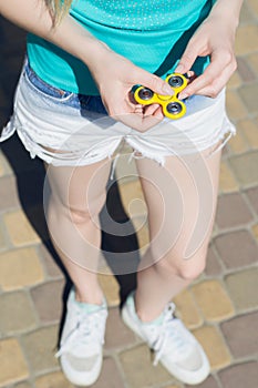 Young girl holding fidget spinner in hands while having a walk outdoors addiction game gamer play player yellow thing toy cropped