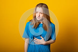 Girl holding her stomach and frowns. Teenage girl has a stomach ache. Female writhes in pain