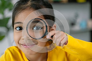 A young girl is holding a magnifying glass and looking at something