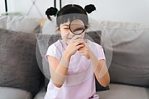 A young girl is holding a magnifying glass and looking at something