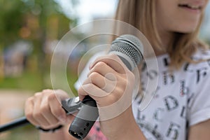 Young girl holding mic with two hands. Microphone and girl singer close up. Cropped image of female teen singer in park
