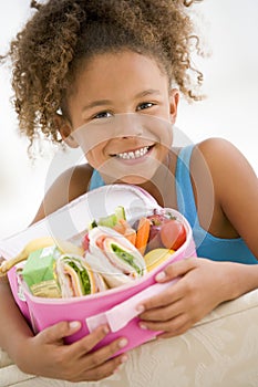 Young girl holding packed lunch in living room