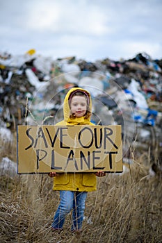 Young girl holding placard, protest sign, standing standing on landfill, large pile of waste, nature pollution