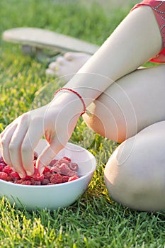 Young girl holding a plate of raspberries, sitting on green grass, summer, dessert