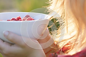 Young girl holding a plate of raspberries, sitting on green grass, summer, dessert