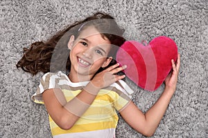 Young girl holding red plush heart lying on the carpet