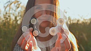 Young girl holding and rotates in the rays of the evening sun a white and black fidget spinners outdoors.