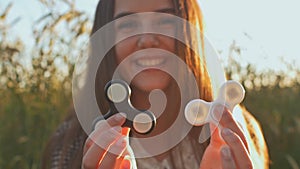 Young girl holding and rotates in the rays of the evening sun a white and black fidget spinners outdoors.