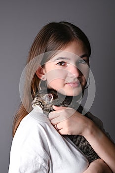 Young girl holding a sleeping baby cat on gray background. Female hugging her cute kitty. Adorable domestic pet concept.