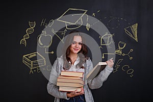 Young girl holding a stack of books, standing by a board with signs of ideas, science and knowledge.