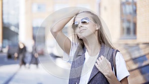 A young girl is holding sunglasses outside fixing her hair