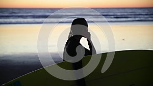Young girl holding surfboard on the beach. Woman walking with surf along the coast. Silhouette of the woman. Beautiful