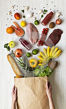 Young girl holds full paper bag of groceries on white wooden table, overhead view. From above. Top view. Flat lay