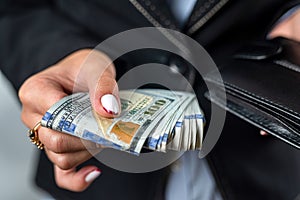 young girl holds a large sum of dollars in her hands and counts money in a black purse.