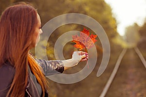 A young girl holds a maple leaf in an autumn forest