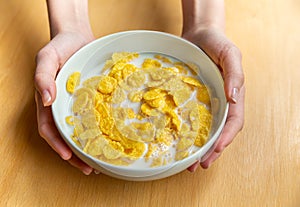 Young girl holds plate with milk and corn flakes