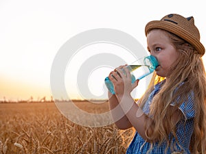 Young girl holds reusable bottle in hands drinks water in wheat field. Pure mineral water advertisement.Active lifestyle.