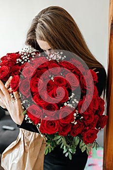 A young girl with a huge bouquet of red roses. Happy woman smelling flowers. Gifts for holidays and birthdays