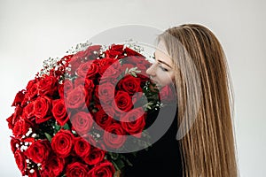 A young girl with a huge bouquet of red roses. Happy woman smelling flowers. Gifts for holidays and birthdays