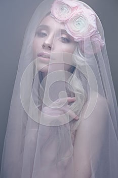 A young girl in the image of a bride with a veil on her face. Beautiful model with a wreath of flowers on her head