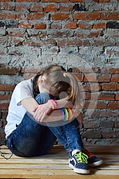 Young girl in jeans and white T-shirt is sitting on the floor and crying. Concept of a non happy and sad teenager