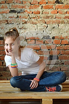 Young girl in jeans and white T-shirt is sitting on the floor and smiling. Concept portrait of a pleasant friendly happy teenager