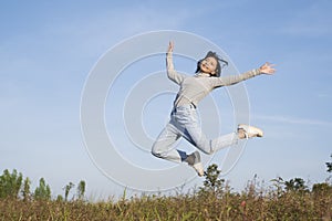 Young girl jumping at field grass with blue sky