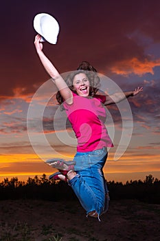 Young girl jumping from happiness up against evening sky