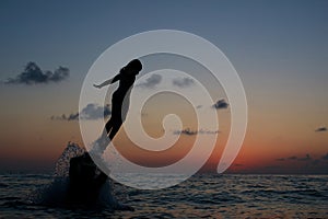 Young girl jumping in the sea beach against sunset sky with sun and clouds. Happy family having fun on sea beach