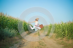 Young girl jumping with suitcase on road in corn