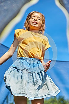 A young girl jumping up and down on her trampoline outdoors