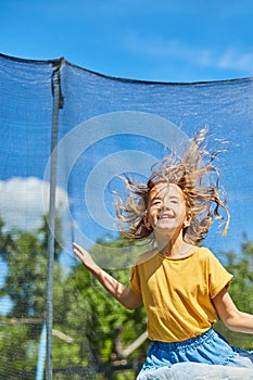 A young girl jumping up and down on her trampoline outdoors