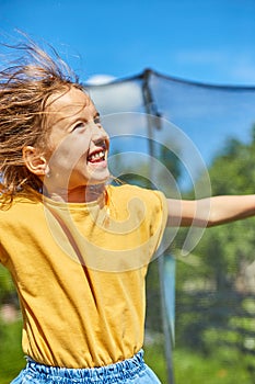 A young girl jumping up and down on her trampoline outdoors