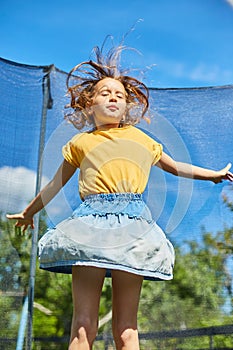 A young girl jumping up and down on her trampoline outdoors