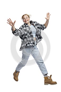 A young girl jumps funny. Cute laughing blonde girl in jeans, blue top and plaid shirt. Activity, energy and positivity. Isolated